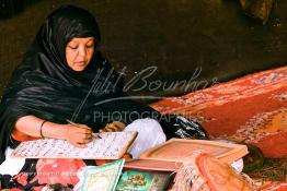 Image du Maroc Professionnelle de  Sous une tente, une femme (institutrice) écrit sur une planche les versets du saint coran, cette photo nous  découvre la méthode traditionnelle de l’enseignement et l’apprentissage du saint coran prodigués aux enfants. Samedi 18 septembre 2004, aux environ de Tan Tan dans un site désertique sur lequel la ville, a toujours accueilli la majorité des tribus et des grandes familles nomades du désert lors d'un grand Moussem, danses chants, course de chameaux et fantasia font partie des festivités. (PHOTO/Abdeljalil Bounhar)
 